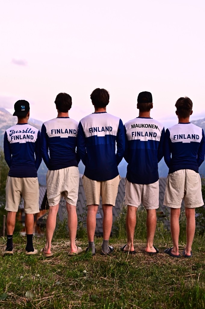 Finnish national team riders in matching Finland jerseys, looking out over mountains.