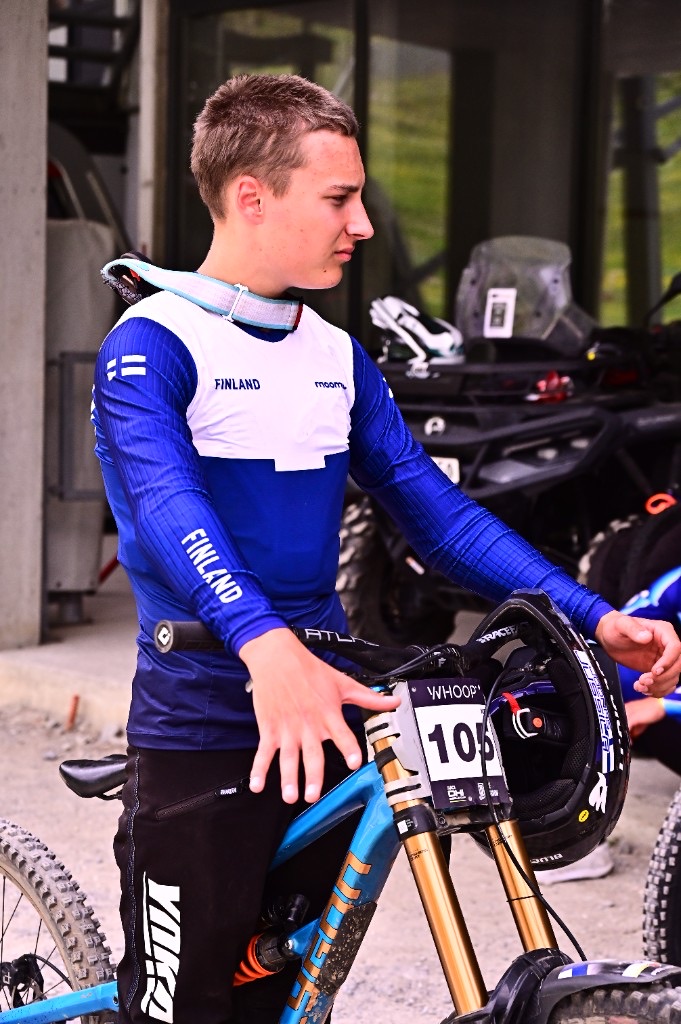 A Finnish junior downhill racer with World Cup number plate 105, standing with his bike before a run.